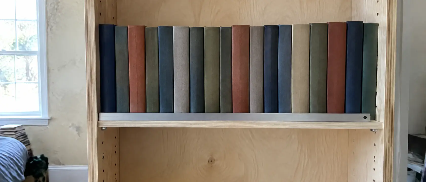 Plywood bookcase side with drilled pin holes and steel pins holding a long shelf of hardbacks that shows no sag