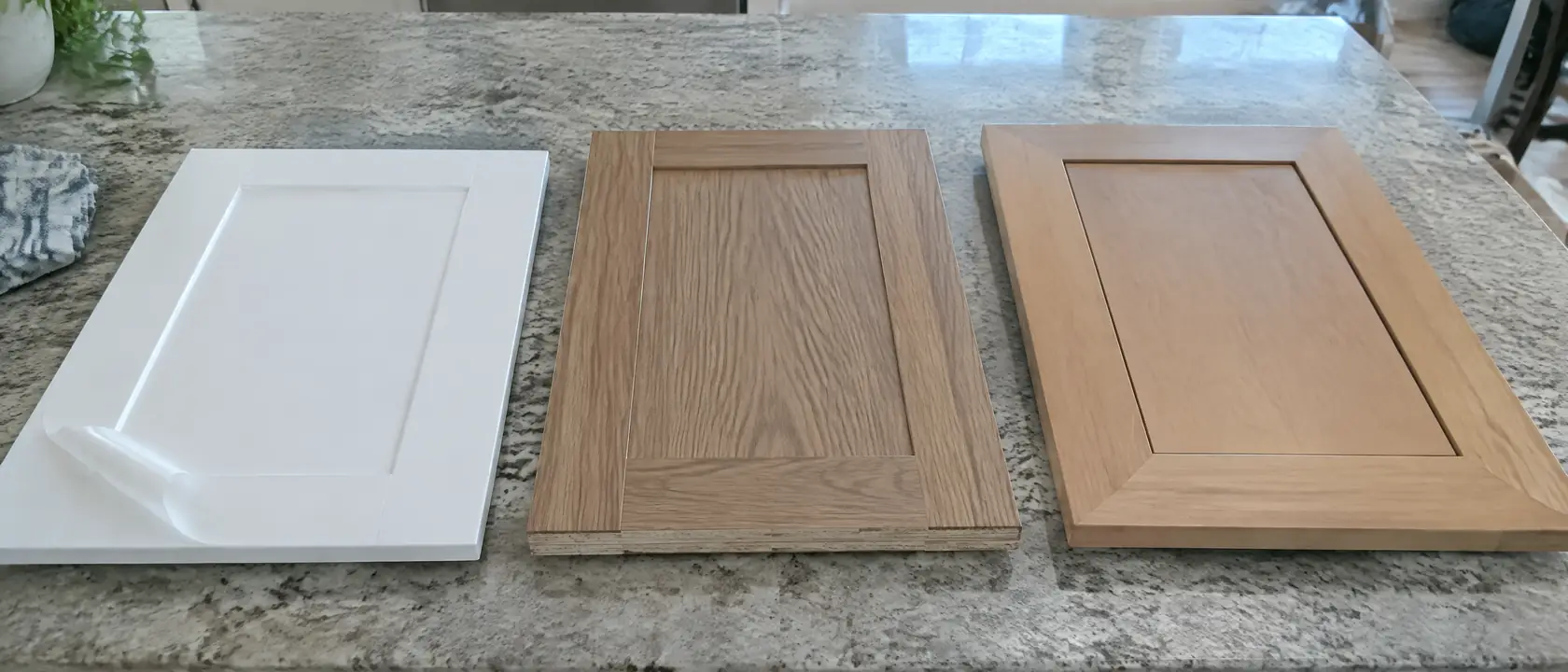 A peeling plastic-skinned door, a wood veneer door and a solid shaker door laid side by side on a kitchen counter
