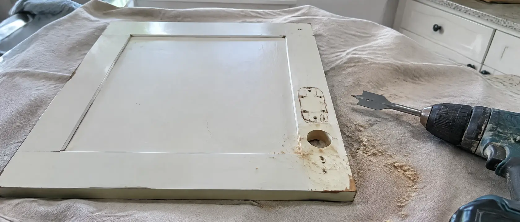 Back of an old painted cabinet door with a new round hinge cup hole bored beside the marks of an old surface hinge