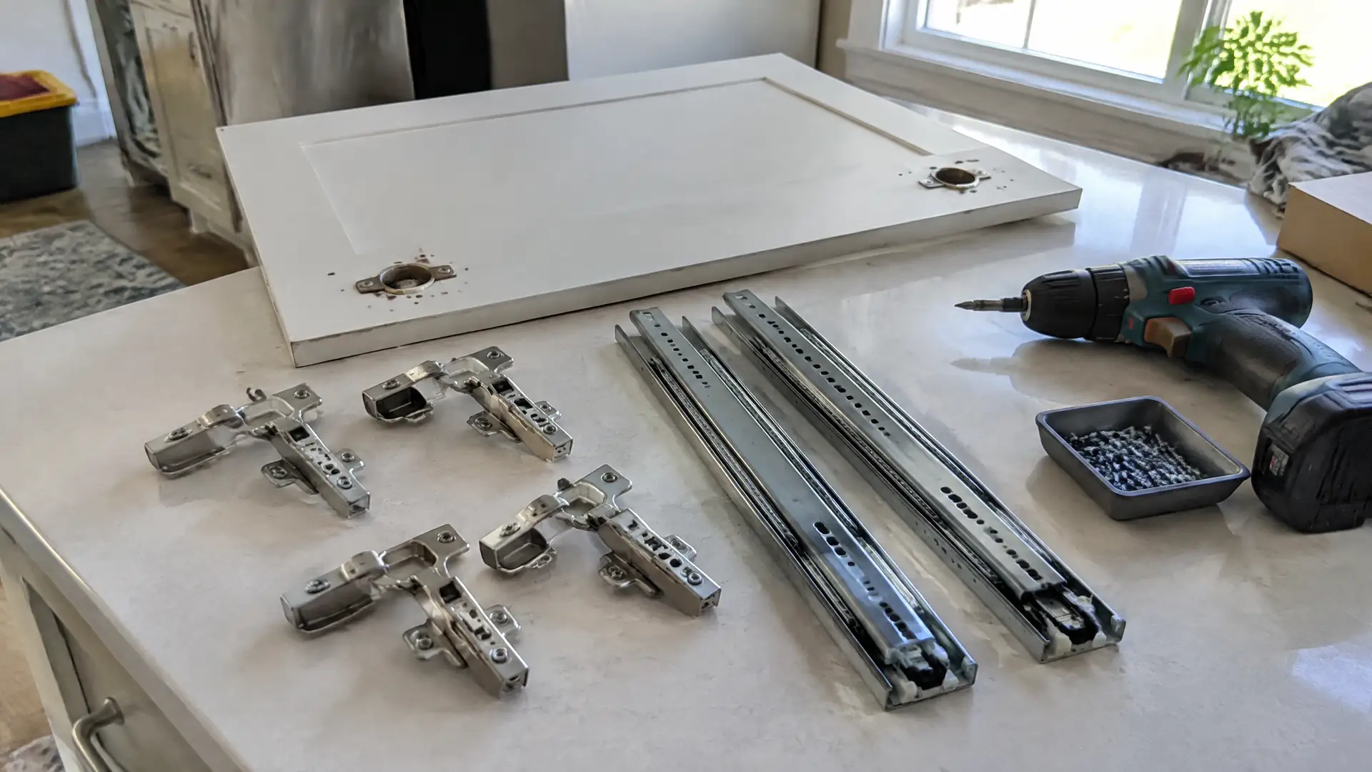 Concealed cabinet hinges and ball-bearing drawer slides laid out on a counter beside a cordless drill