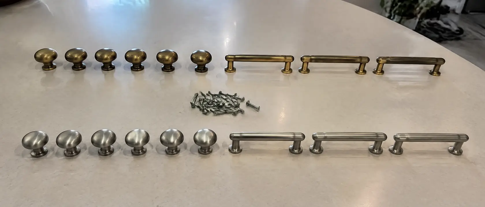 Aged brass and satin nickel cabinet knobs and pulls laid out in rows on a bench
