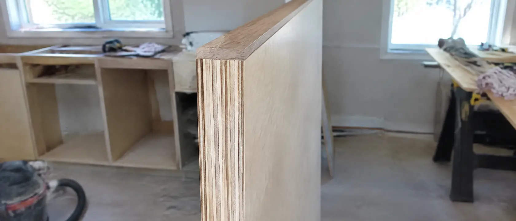 The cut edge of a sanded plywood cabinet panel with hardwood edge banding trimmed flush