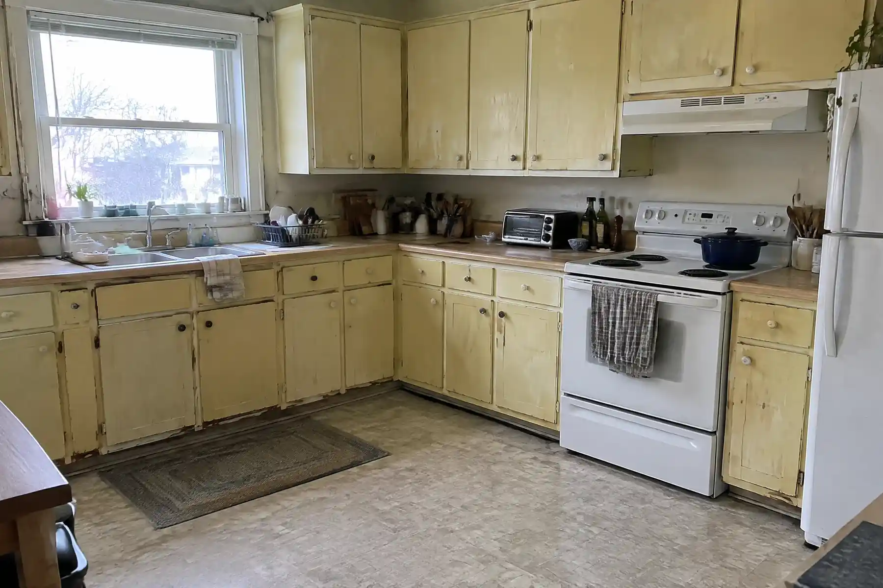 An L-shaped kitchen with thick yellowed paint and chipped door edges before repainting