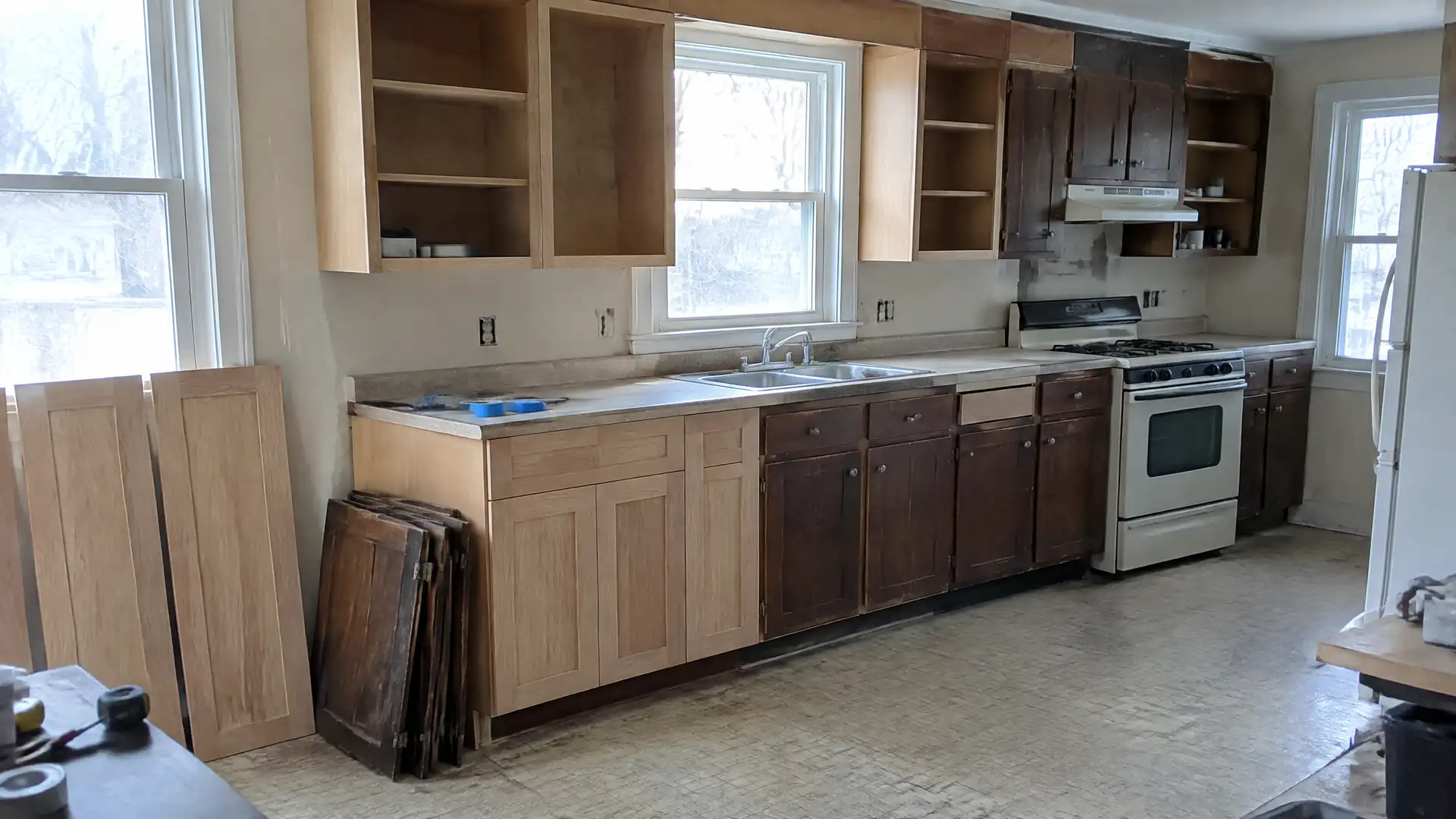 A kitchen partway through a reface, with new oak fronts on the left run, the old dark cabinets still on the right and the old doors stacked on the floor