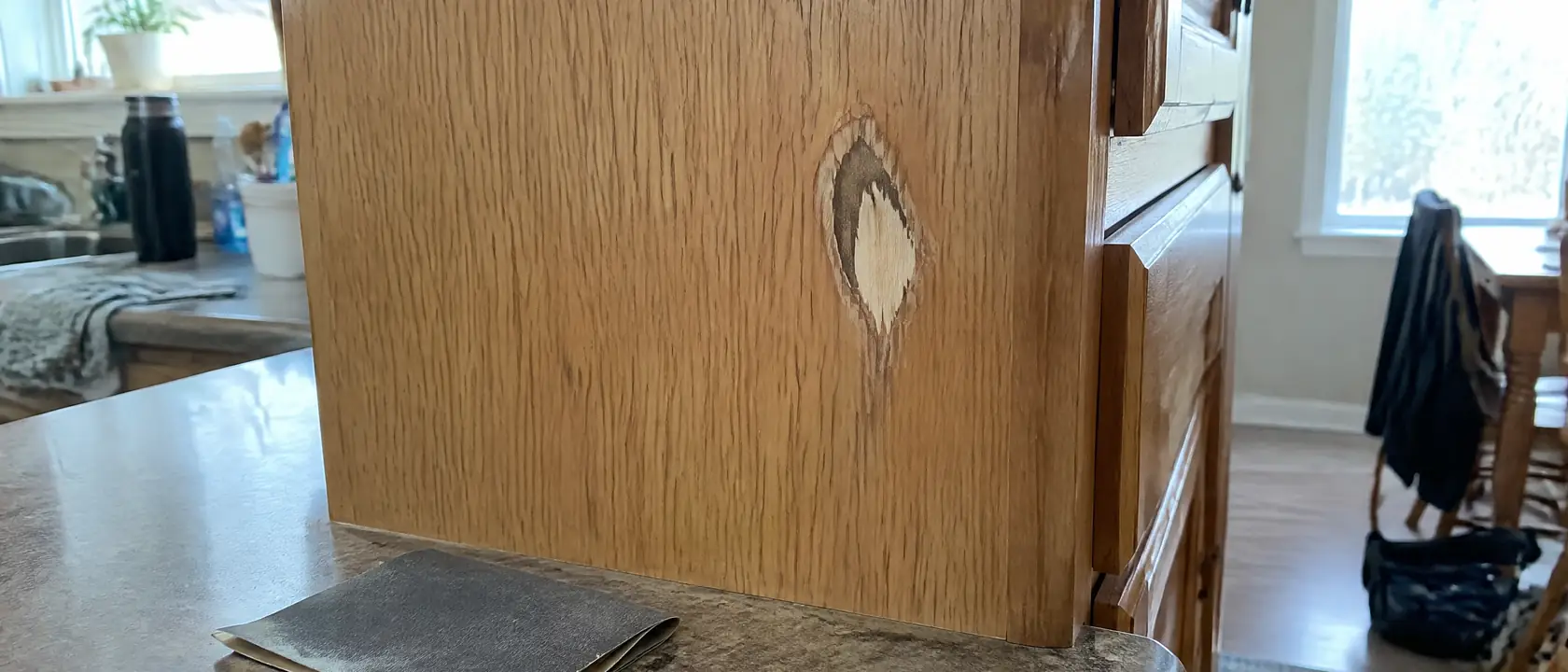 Kitchen cabinet end panel sanded through its thin oak veneer, a dark glue line showing in one worn patch