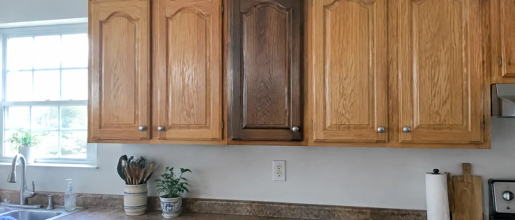 Honey oak kitchen cabinets with one sample door rehung in a darker brown stain, the oak grain still visible