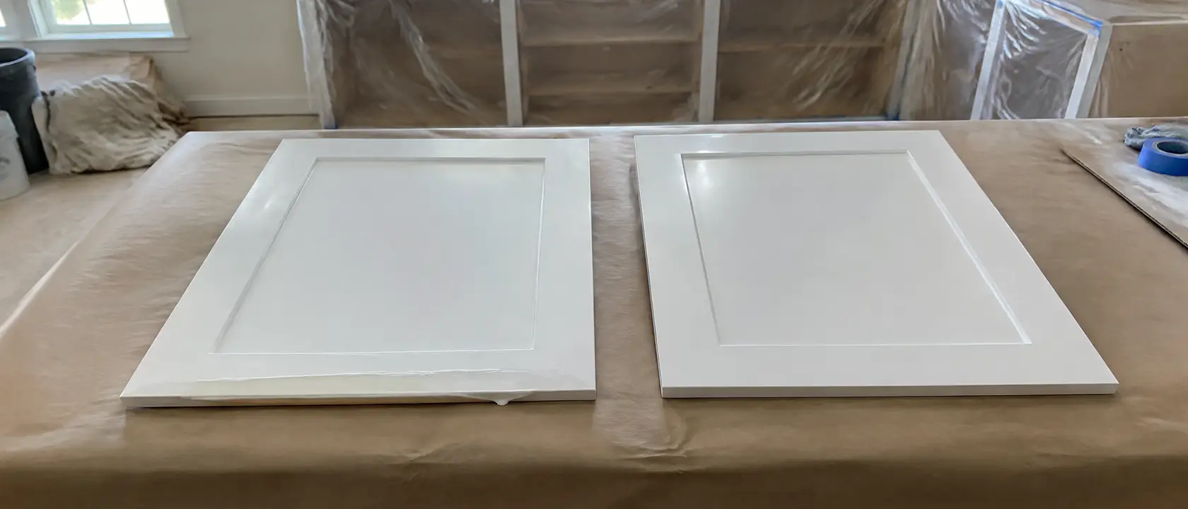 Two white cabinet doors on a covered counter, one with a finish run and trapped dust, the other sprayed smooth