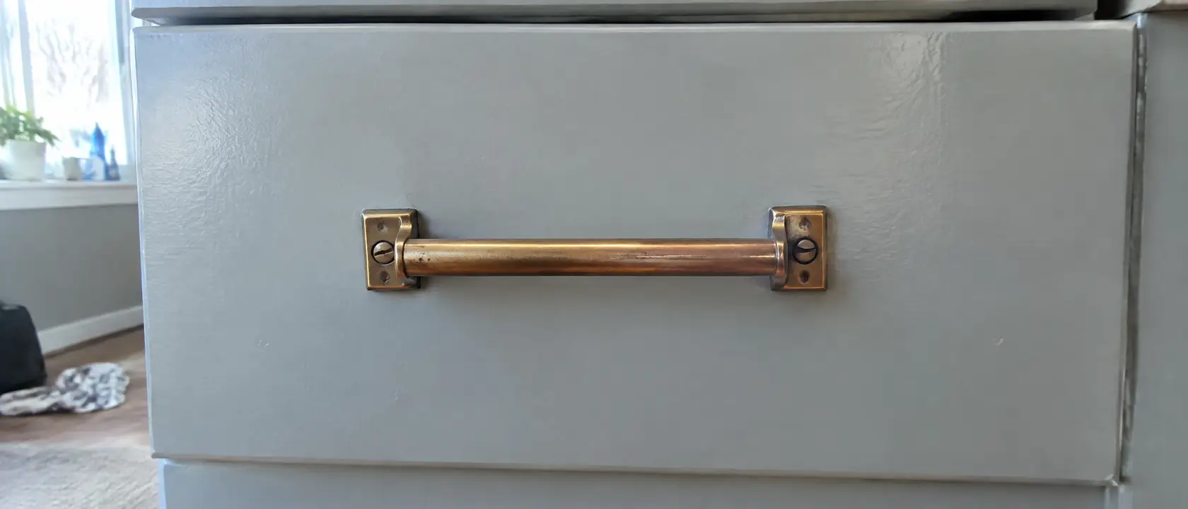 An aged brass bar pull fixed square to a painted drawer front