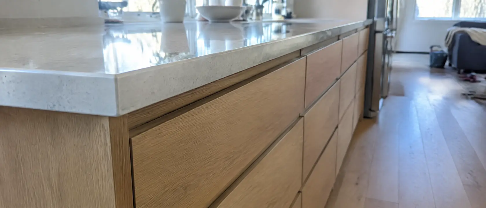 The edge of a pale stone counter meeting warm oak drawer fronts with even reveals