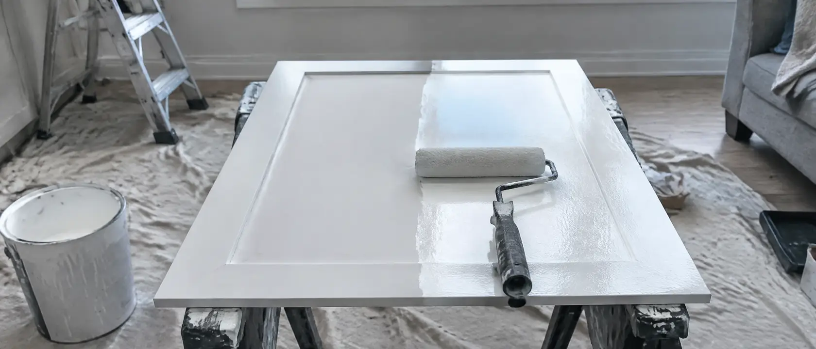 A cabinet door on horses with a soft roller drawn halfway across it in fresh white paint