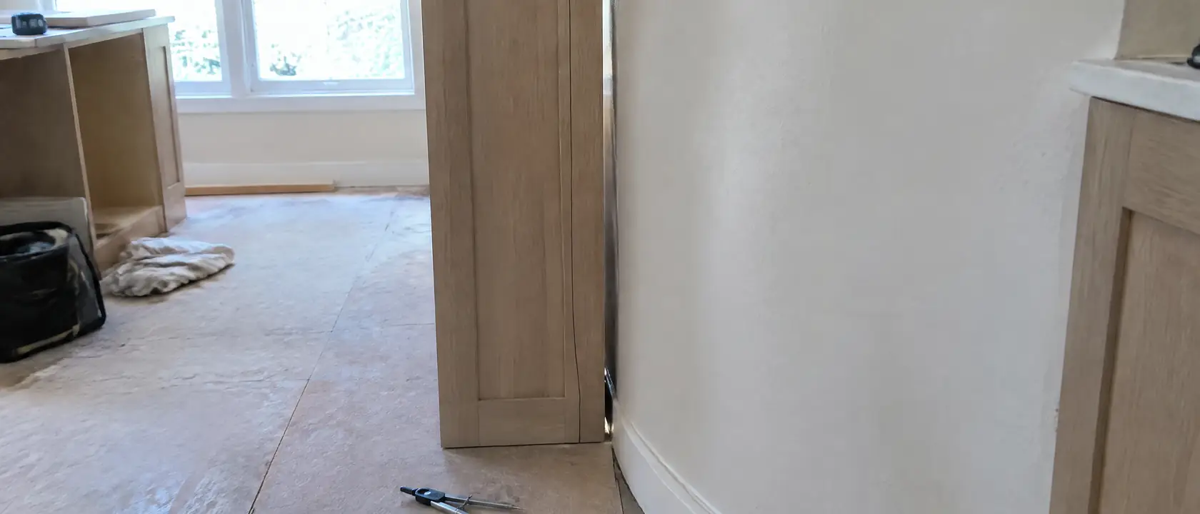 A pencil scribe line drawn down a cabinet stile held against a bowed plaster wall