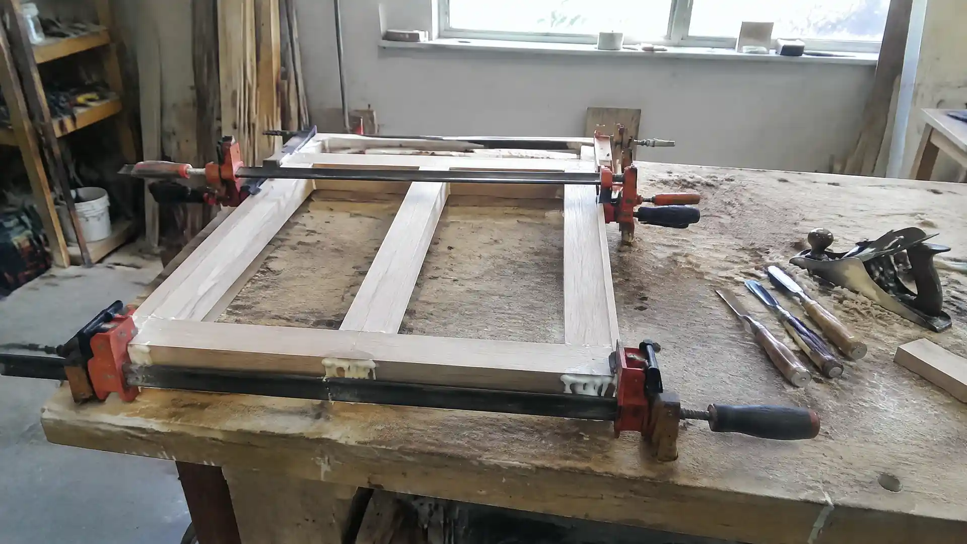 A cabinet face frame clamped up square on a workshop bench with chisels and a block plane alongside