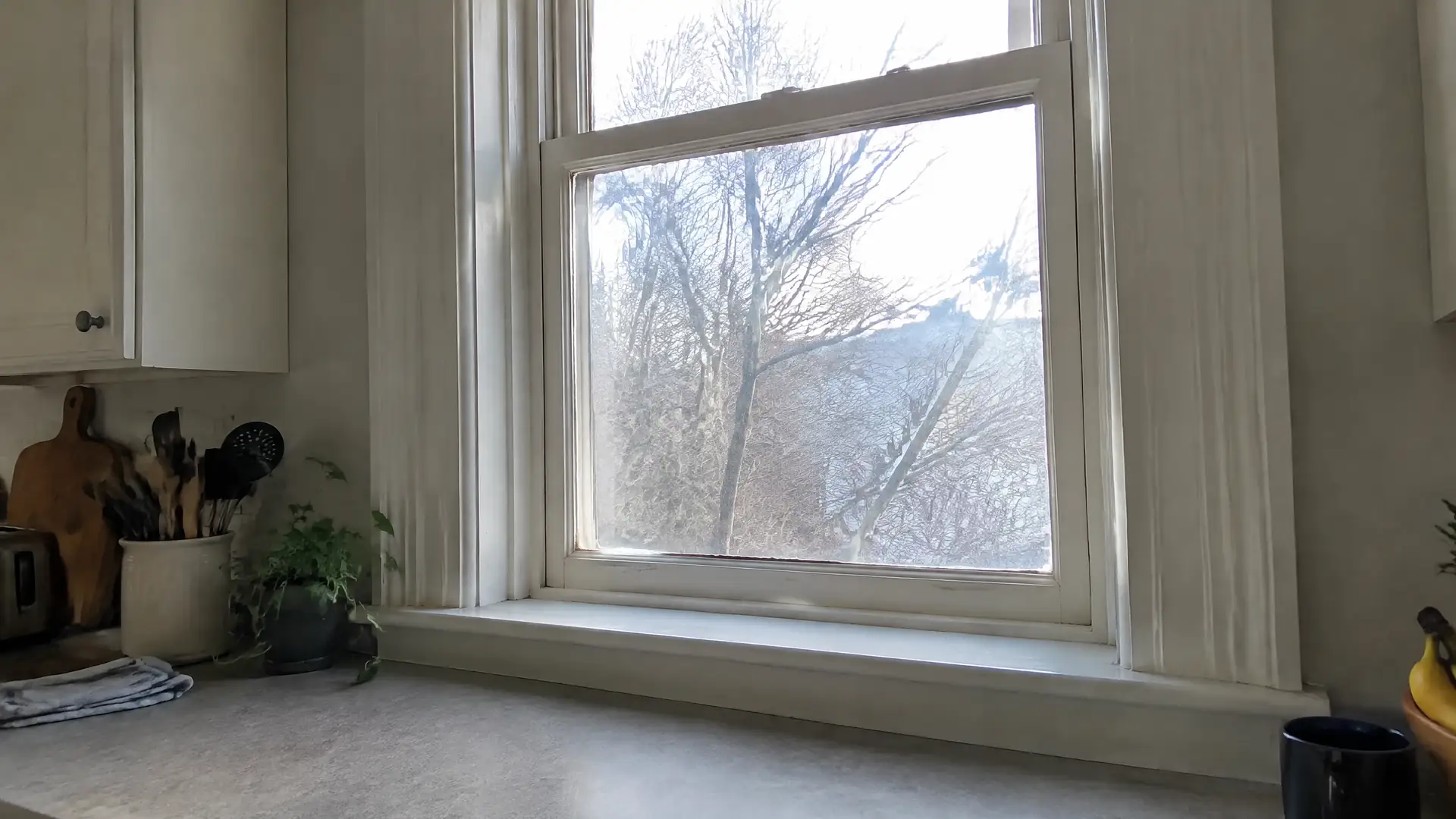 A tall double-hung kitchen window with wavy glass and a deep painted sill in an old house