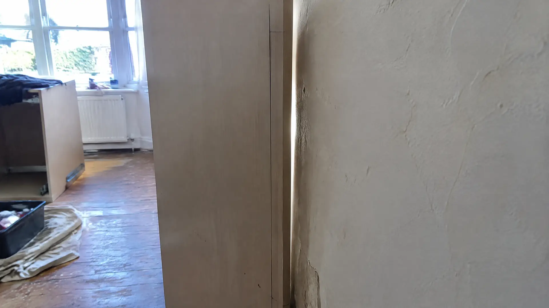 A cabinet side panel held to a bowed plaster wall with a scribe line drawn down the edge