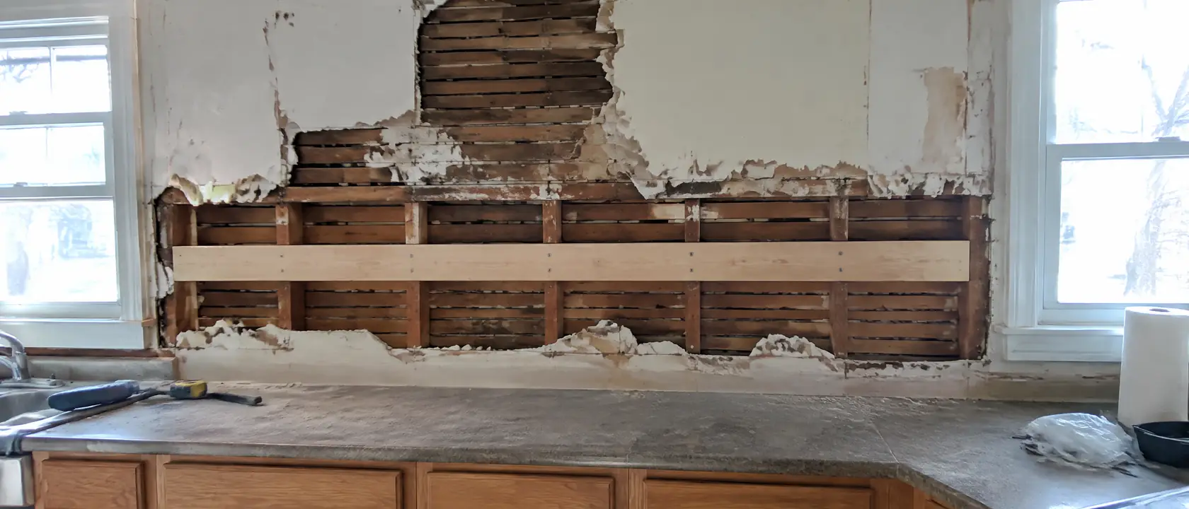 Kitchen wall after old upper cabinets came down, plaster broken back to wood lath and new blocking fixed to bare studs