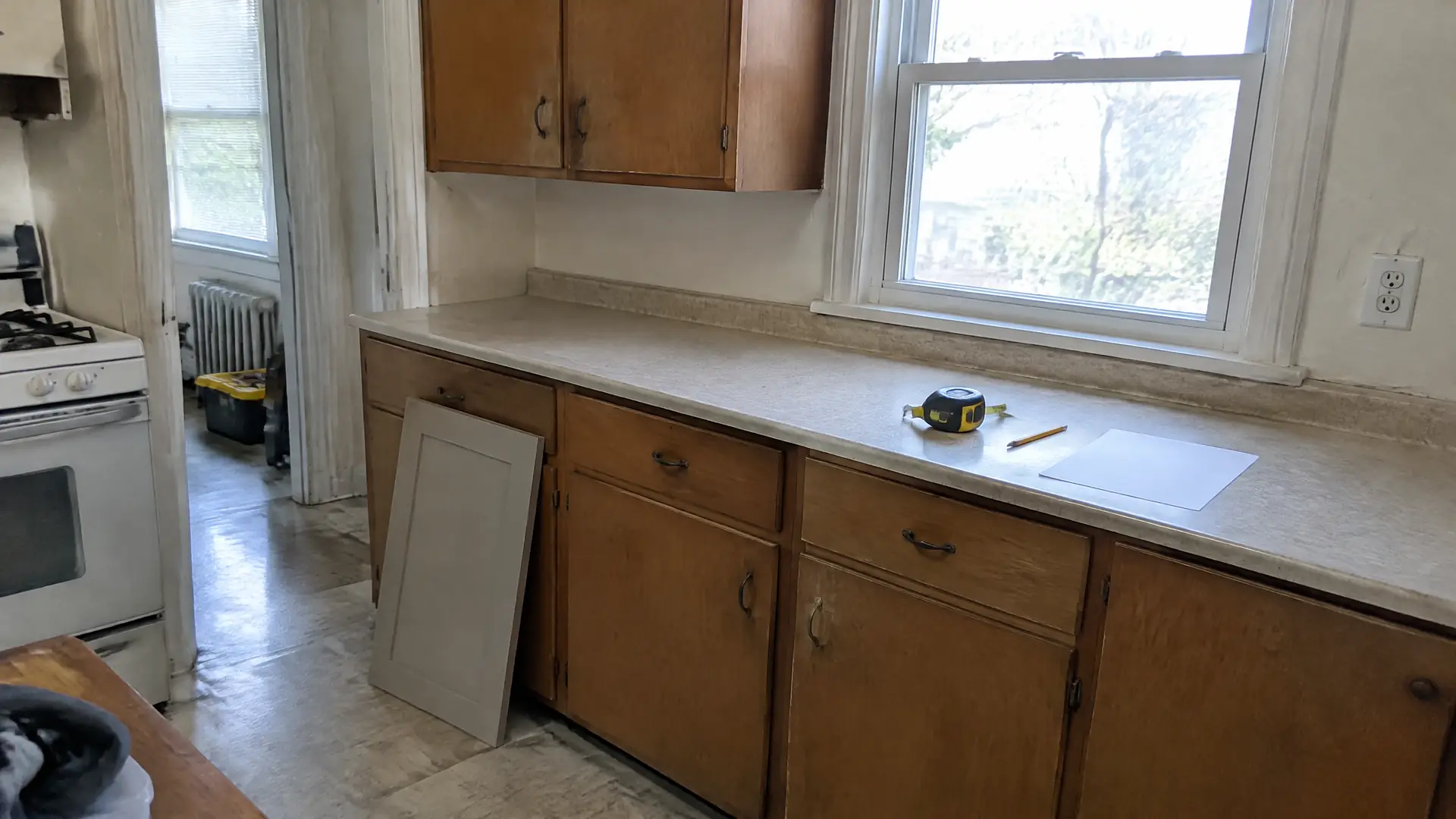 A tape measure, pencil and sample cabinet door on the counter of an older kitchen during a measure