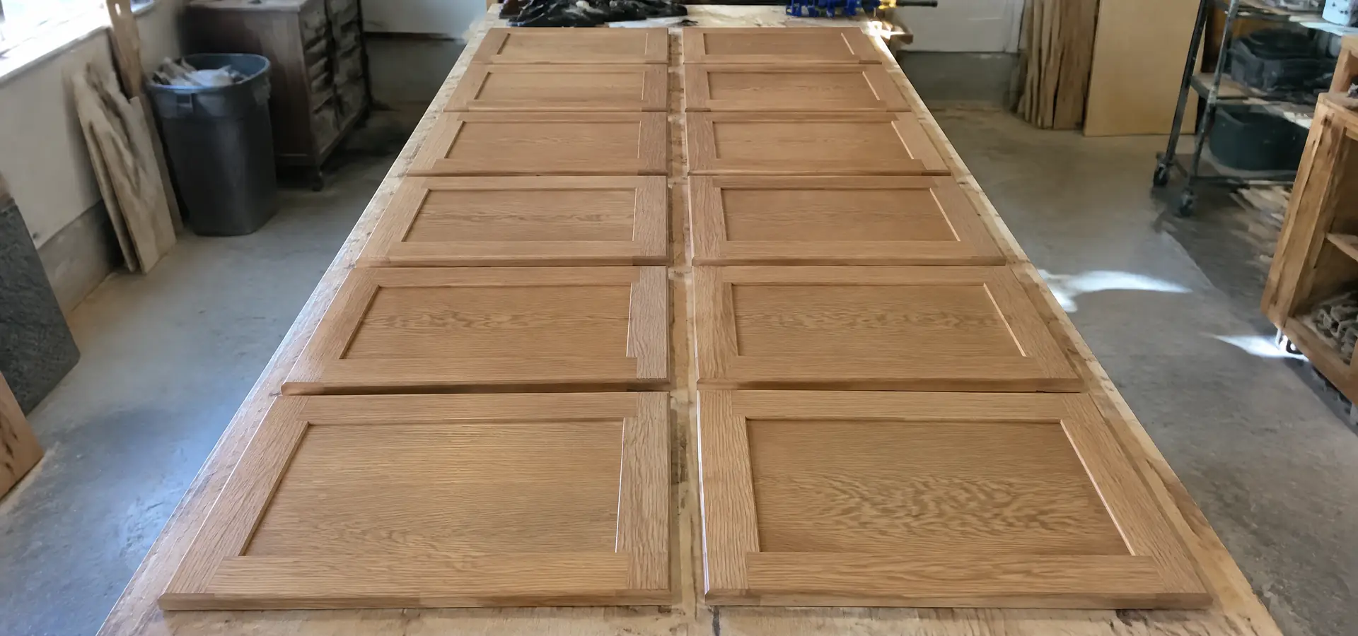 Finished white oak cabinet doors laid in rows on a workshop bench before hanging