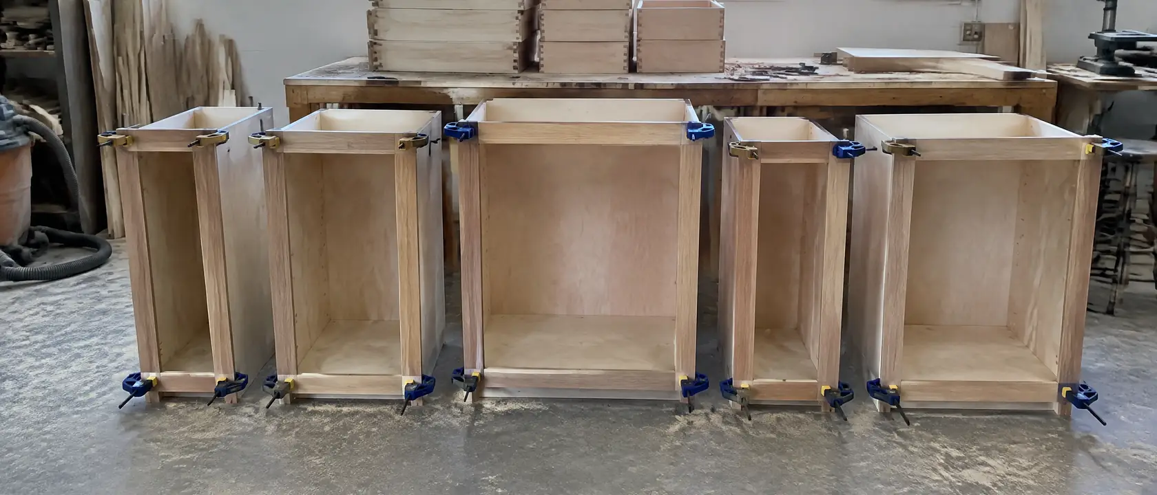 Plywood cabinet boxes in different widths with solid wood face frames clamped on, dovetailed drawers stacked behind