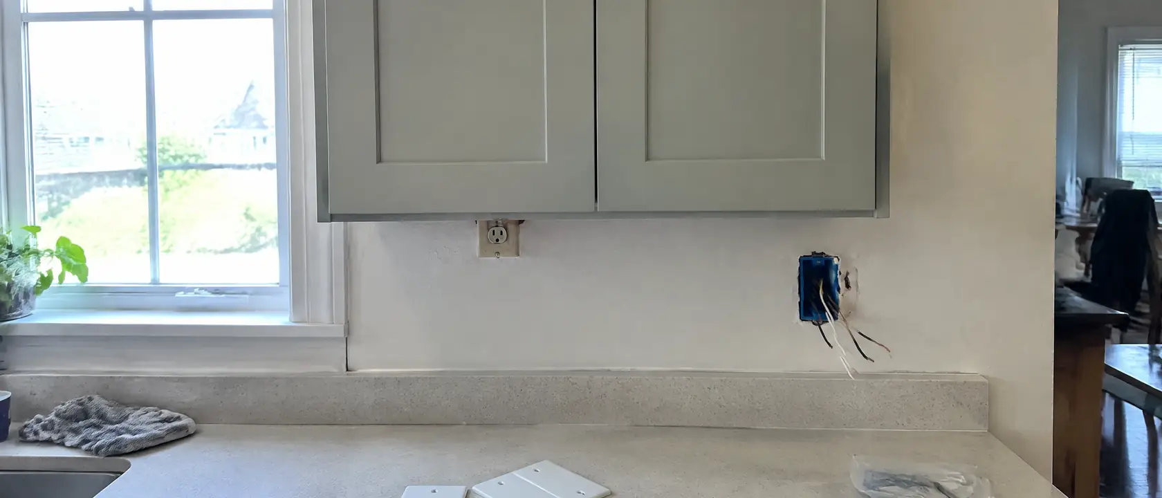 New wall cabinet partly covering an old outlet, with a fresh outlet box cut into the plaster further along the backsplash