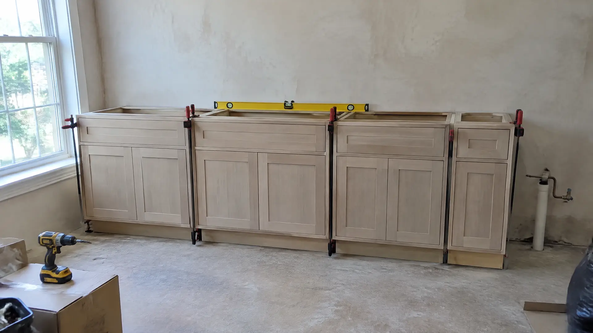 New base cabinets shimmed and clamped against a bare plaster wall during a Lynn kitchen install