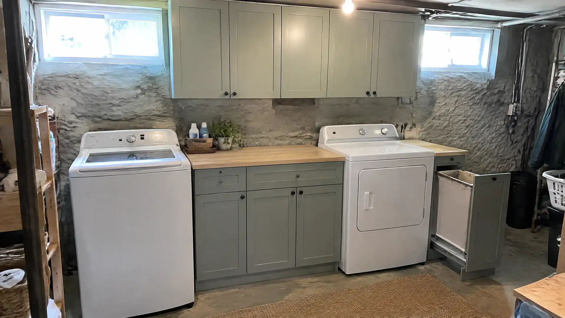 Painted laundry cabinets and a butcher-block counter between the washer and dryer in a stone-walled basement