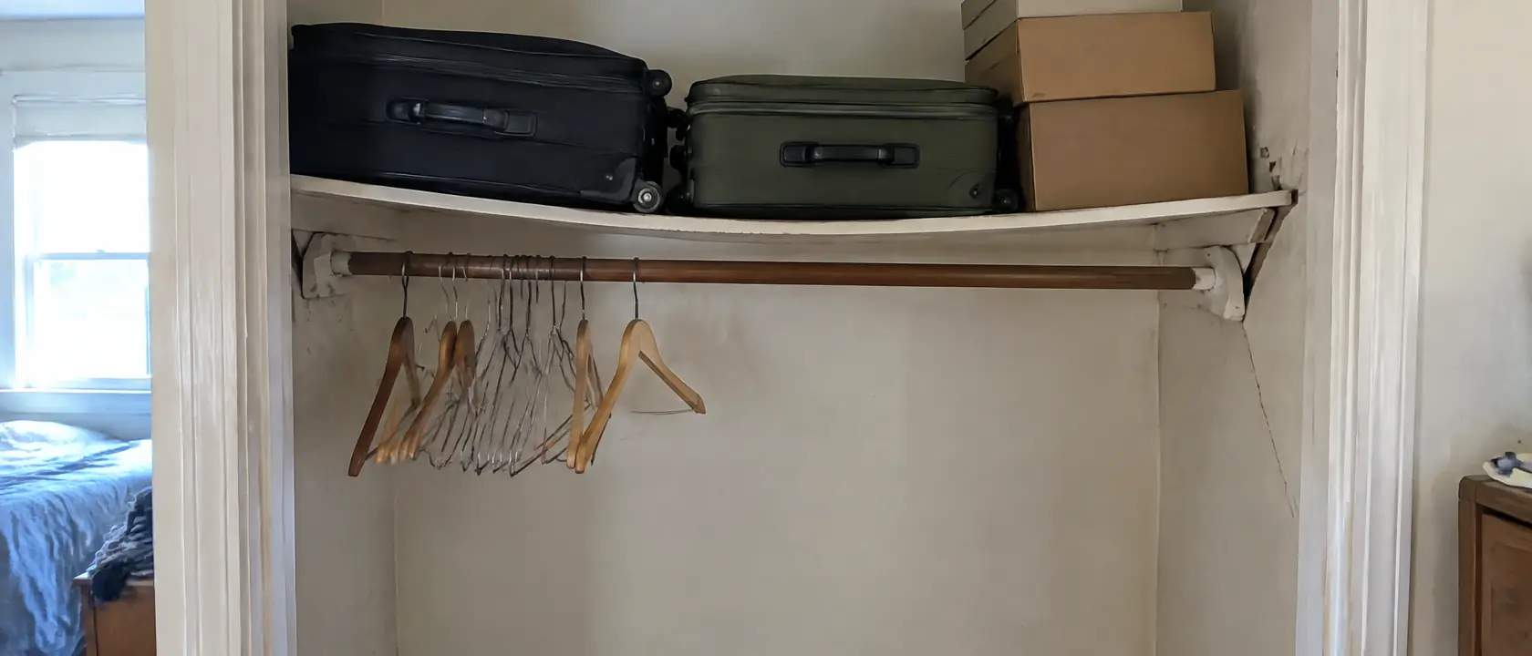 Original painted closet shelf bowed under suitcases and boxes, its support cleat pulling away from cracked plaster