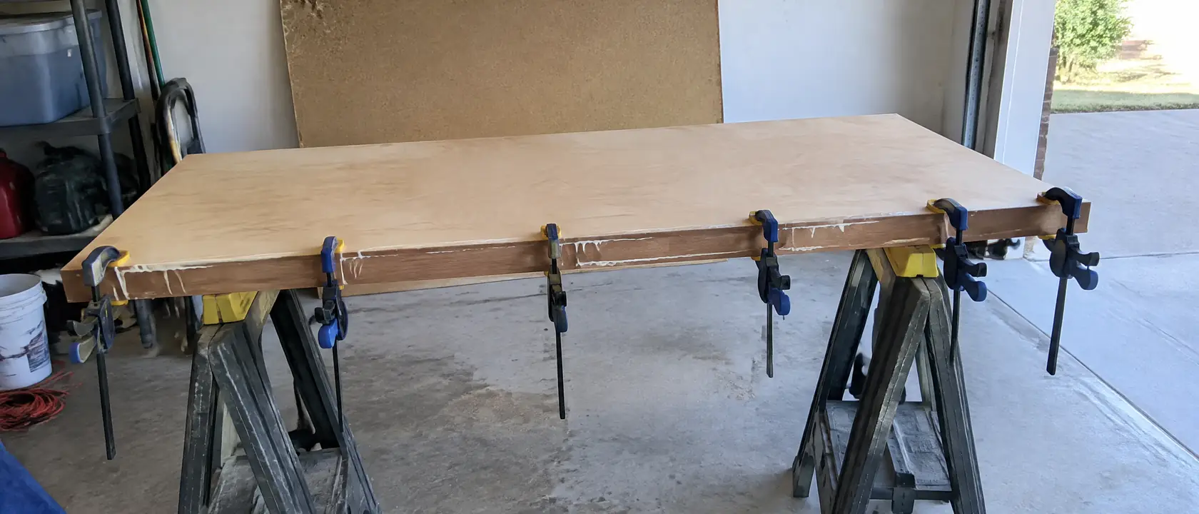 Hardwood strip being glued and clamped to the front edge of a plywood shelf, an old thin particleboard shelf behind