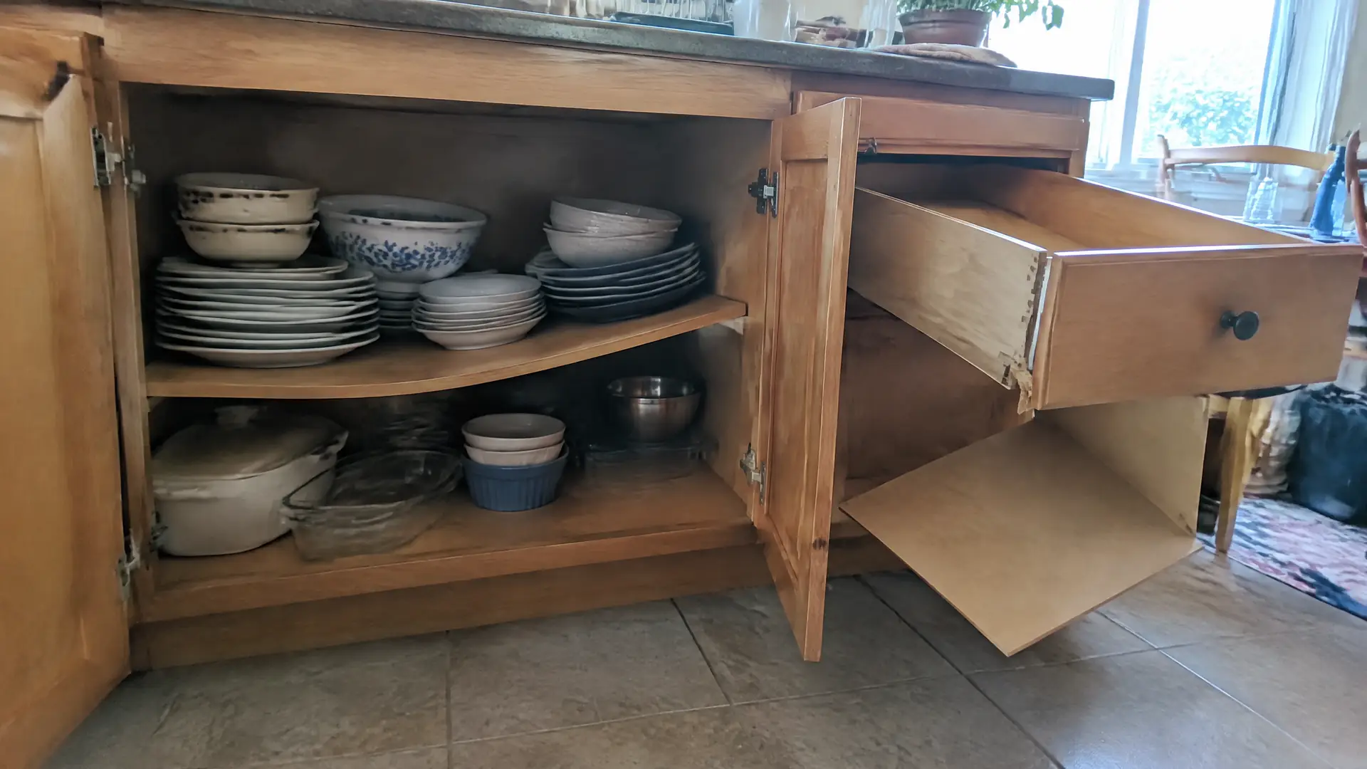 A cabinet shelf bowed under stacked crockery beside a drawer with its bottom panel dropped free