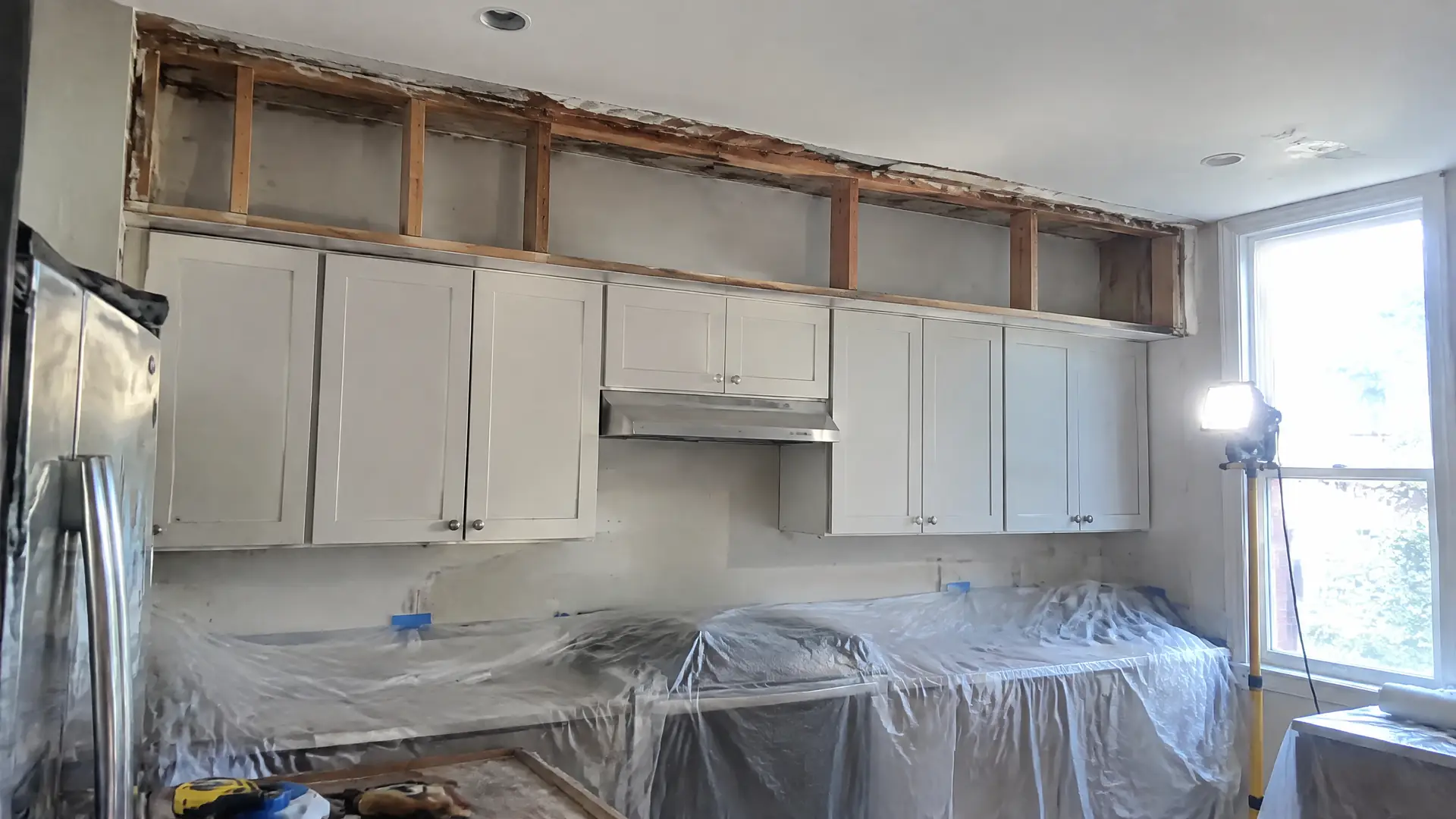 A boxed soffit opened above wall cabinets showing framing and the old plaster edge