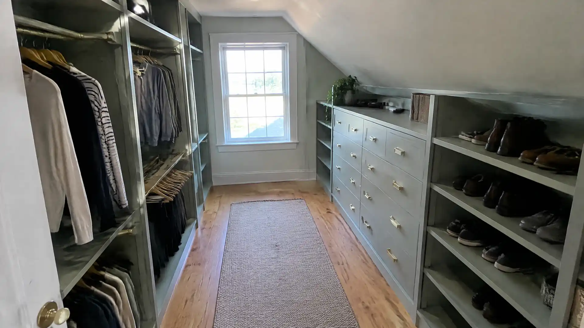 A walk-in closet fitted in painted cabinetry with two rail heights, scribed under a sloped ceiling