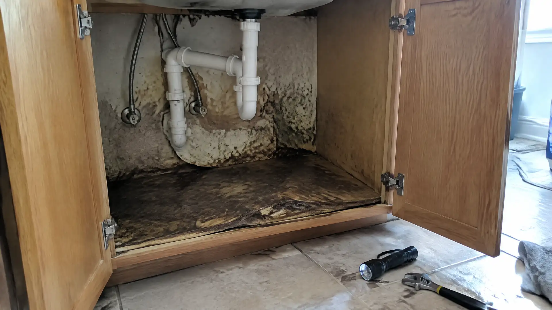 A sink base cabinet floor swollen and blistered dark under a slow supply leak