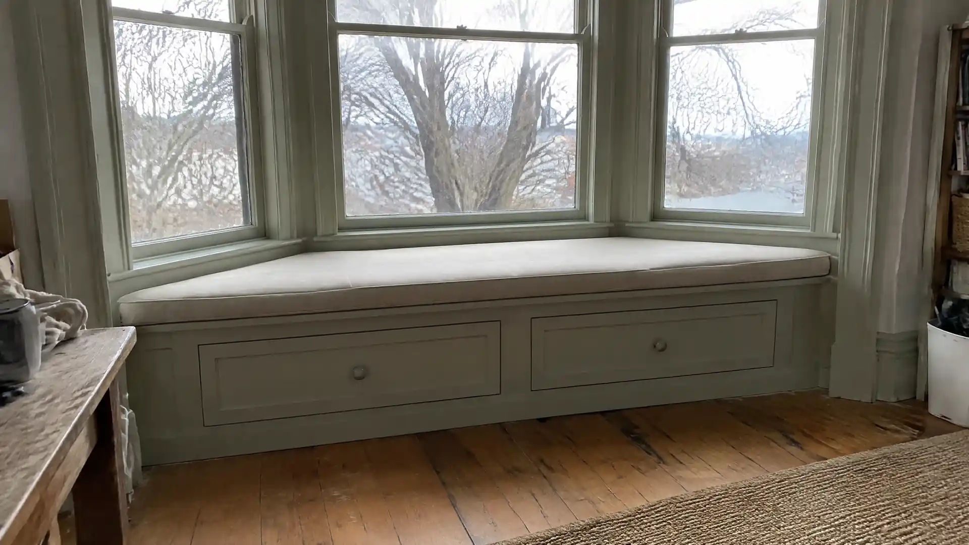 A built-in bay window bench with two deep storage drawers, painted to match old trim